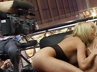 Arousing lesbian blonde with big tits hammering her partner doggystyle with a strapon at the backstage